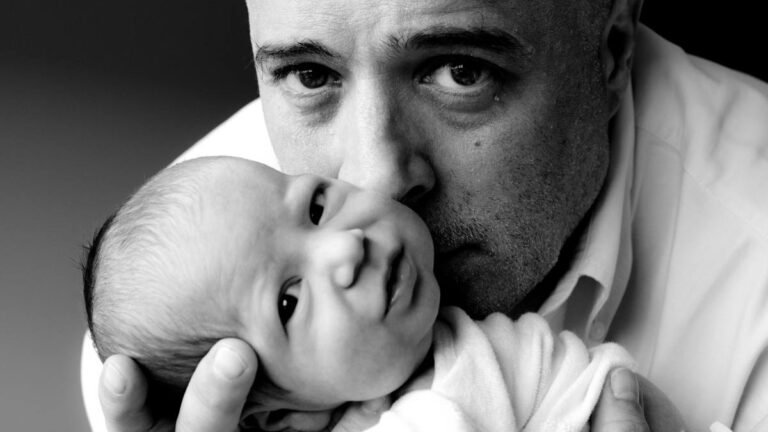 A man gently holds a newborn baby close to his face, looking intently at the camera. The black and white photo highlights their facial expressions and the tender, protective gesture—moments that inspire trust in a DNA court admissible paternity test.